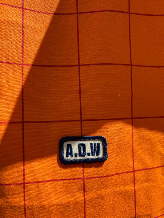 Fokus auf Baumwolltasche mit grafischem Grid-Print in Orange, gesticktem A.D.W. Patch und langen Henkeln – minimalistisches Streetwear-Design.
