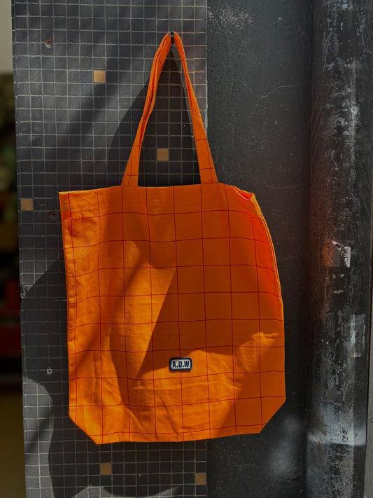 Baumwolltasche mit grafischem Grid-Print in Orange, gesticktem A.D.W. Patch und langen Henkeln – minimalistisches Streetwear-Design.